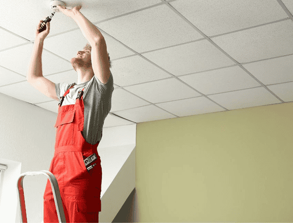 A security installer on a ladder working on ceiling