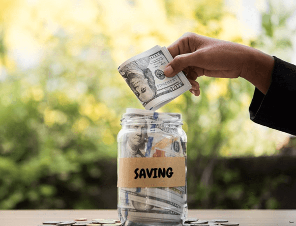 A hand placing money into a savings jar