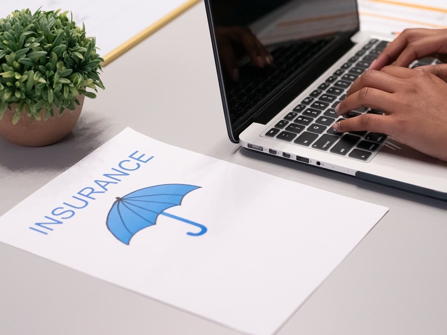 A laptop being used with a piece of paper next to it saying insurance with an umbrella icon